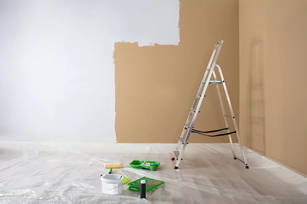 Ein Raum ist mit Malervlies ausgelegt, darauf steht eine Trittleiter und man sieht die halb-gestrichene Wand.