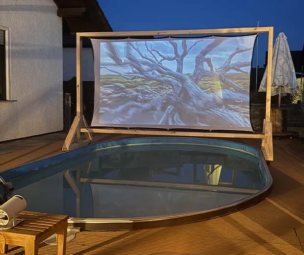 Eine große selbtsgebaute Leinwand steht vor einem Pool auf der Terrasse.