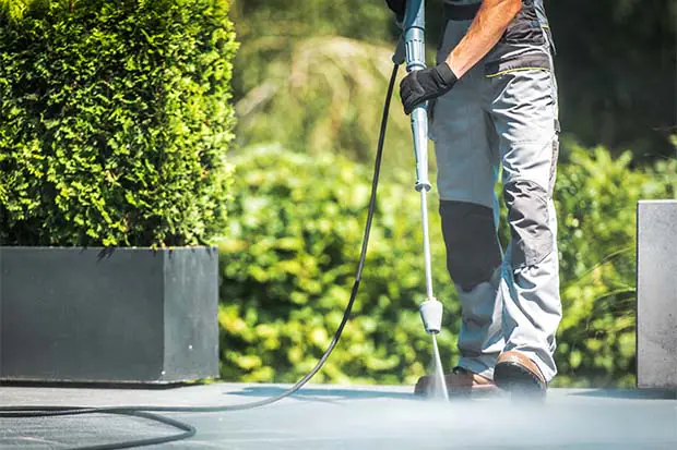 Person reinigt Terrasse im Garten mit einem Hochdruckreiniger an einem sonnigen Tag